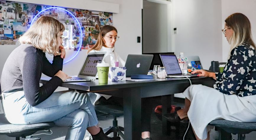 3 women sitting on chair in front of table with laptop computers