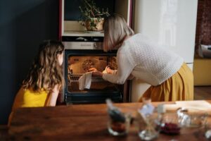 Woman with girl putting baking tray in oven