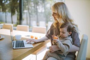 Mother carrying her baby while working on a laptop