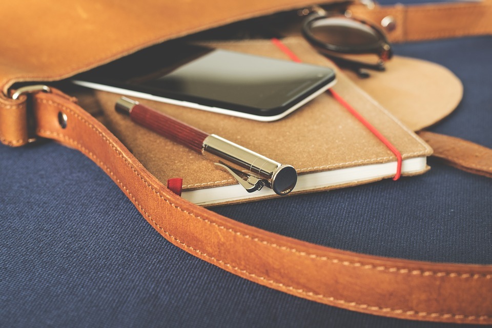 a leather bag with a notebook, a pen and a phone