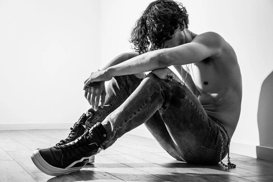 a lonely, shirtless guy sitting on the floor