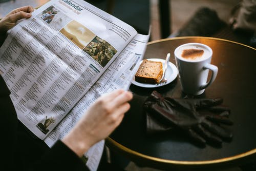 A man reading a newspaper with a mug of coffee