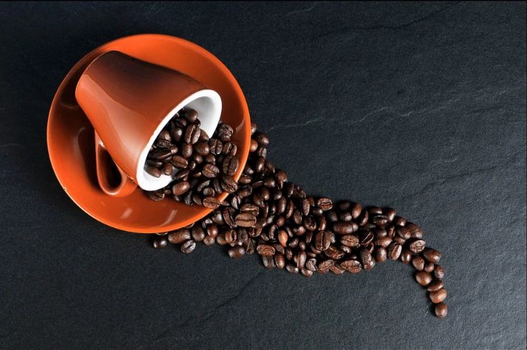 coffee beans spilling out of a coffee cup; a dark grey surface