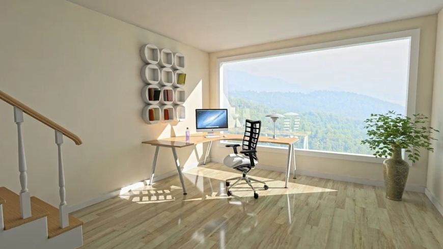 A spacious and clean room, with an L-shaped desk, a monitor, a chair, a vase on the corner, and book shelves on the wall