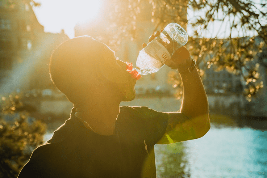 bottled water with red cap, a man wearing a black shirt drinking water, tree leaves I the background