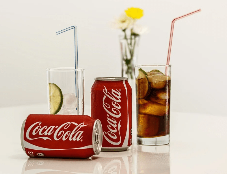 two glasses with straw, two red Coca-Cola bottles, flowers inside a vase