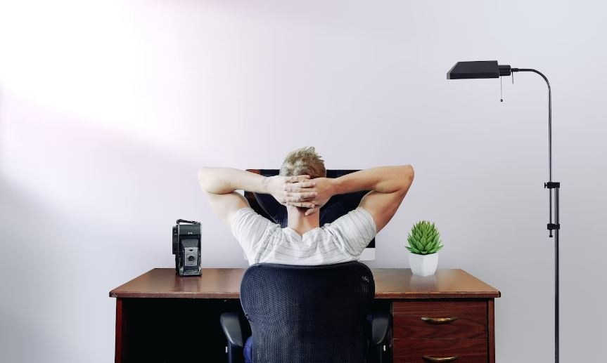 Man holding his head while sitting on a chair near computer desk