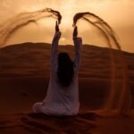 Woman sitting on the desert while playing sand during golden hour – Good health Image